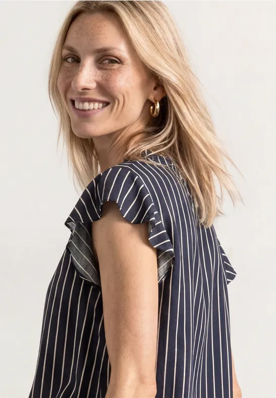 Lächelnde blonde Frau in blau-weiß gestreiftem Top.