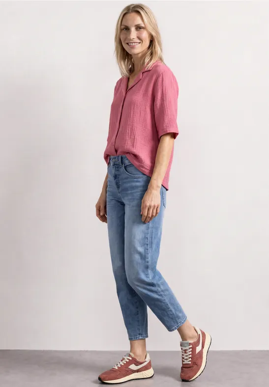 Eine Frau in rosa Bluse und Jeans steht und lächelt