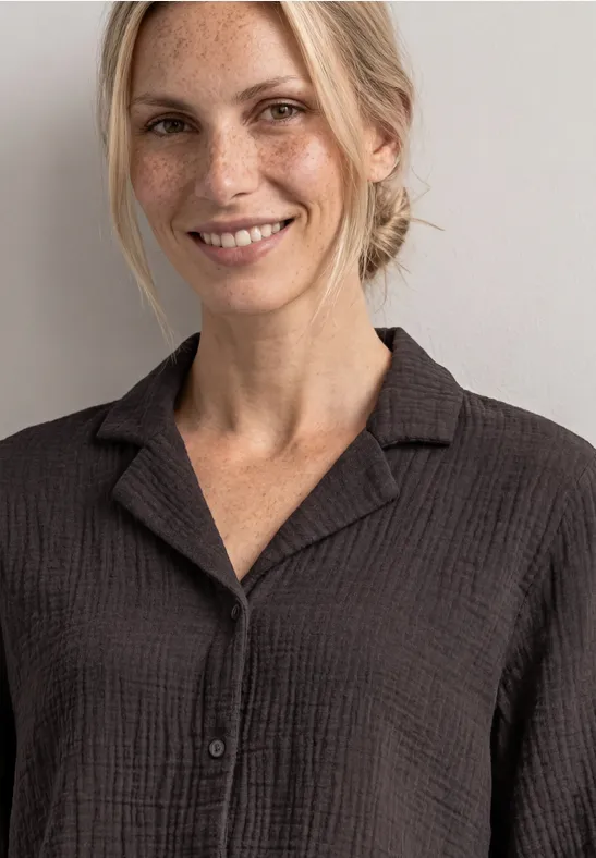 Een lachende blonde vrouw draagt een donkergrijs shirt voor een neutrale achtergrond.