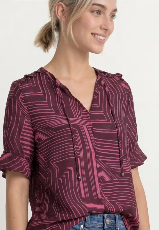 Vrouw met een paarse-roze blouse met geometrisch patroon en korte mouwen.