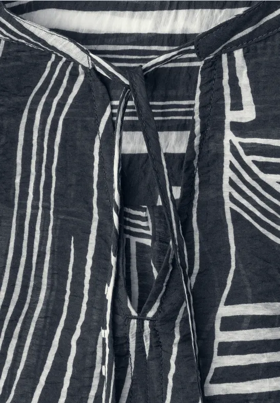 Close-up van een donkerblauw shirt met witte, geometrische strepen en een koordsluiting bij de hals.