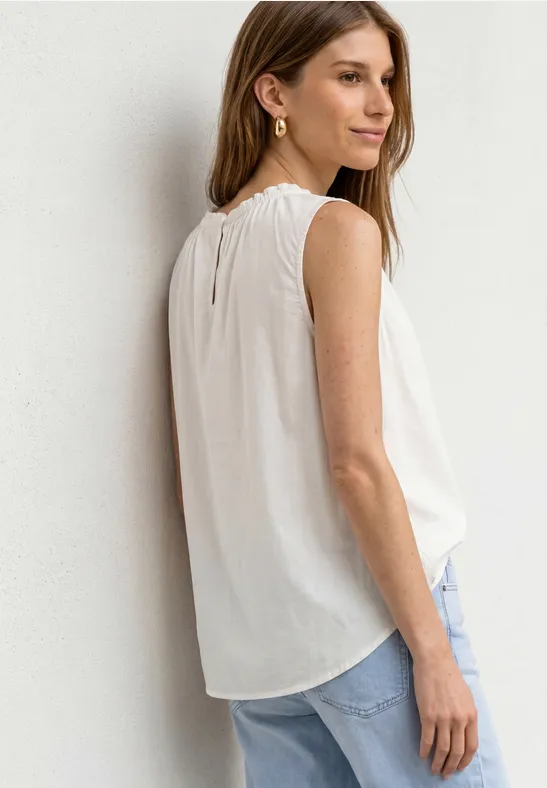 Frau von der Seite in weißem Top und blauen Jeans vor hellem Hintergrund.