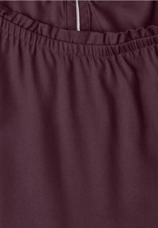 Nahaufnahme eines burgunderfarbenen Kleidungsstücks mit elastischem Bund und Reißverschlussdetail.