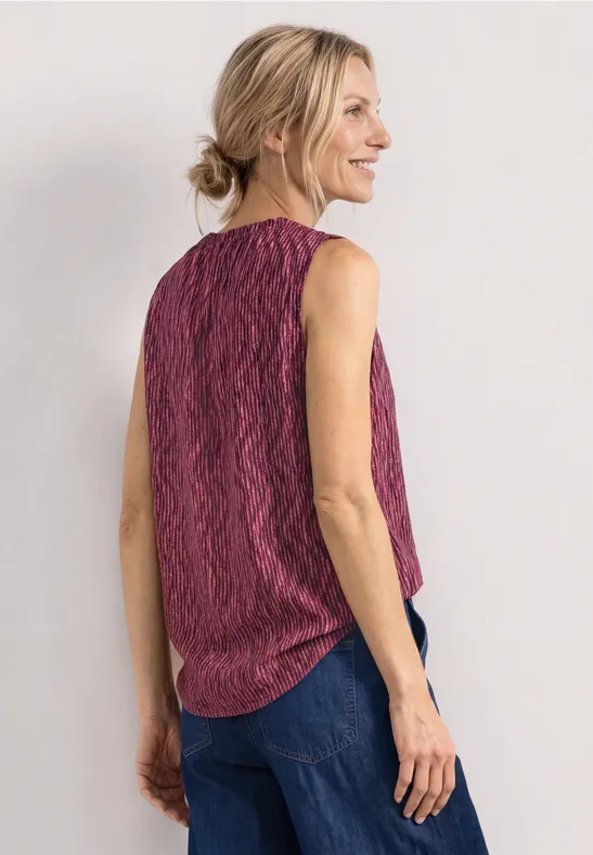 Femme vue de dos, coiffure en chignon, débardeur rose à motif ondulé et jean bleu.