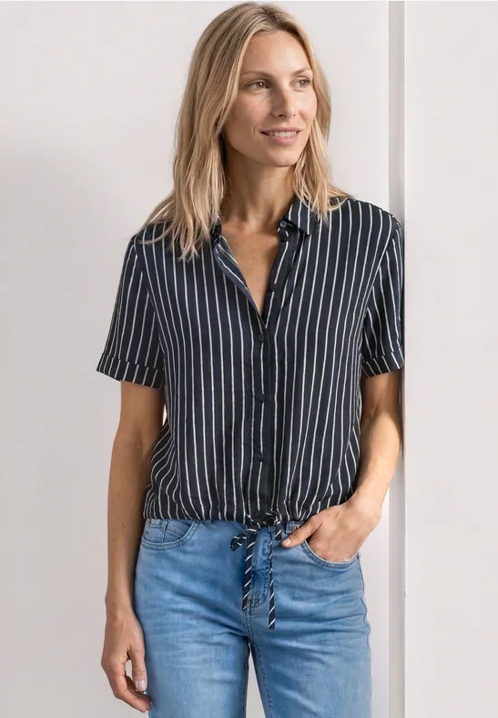 Een vrouw draagt een korte mouw gestreepte blauw-witte blouse geknoopt vooraan met een blauwe jeans.