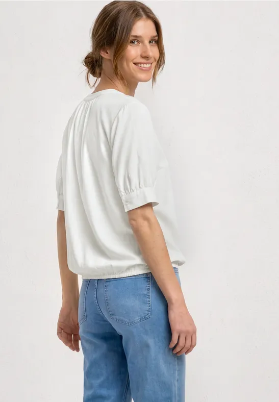 Eine Frau in lockerem weißem Shirt und blauen Jeans, von hinten schräg fotografiert.