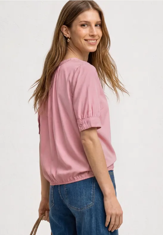 Eine Frau von hinten in rosa Bluse und blauen Jeans, die eine Tasche hält.
