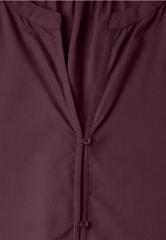 Nahaufnahme einer weinroten Bluse mit V-Ausschnitt und Knopfleiste.