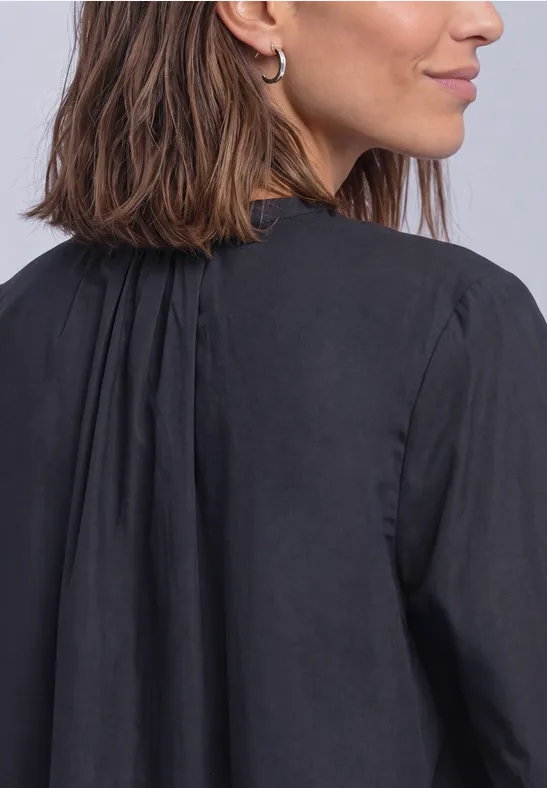 Frau mit schulterlangen braunen Haaren und silbernen Creolen, trägt eine schwarze Bluse, im Profil von hinten.