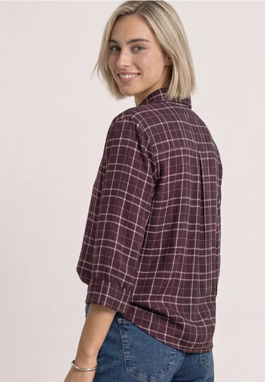 Eine Frau dreht sich über die Schulter, trägt karierte Bluse und Jeans, lächelt.