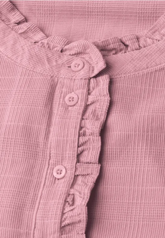 Detailaufnahme einer rosa, strukturierten Bluse mit Rüschenbesatz und Knopfleiste.