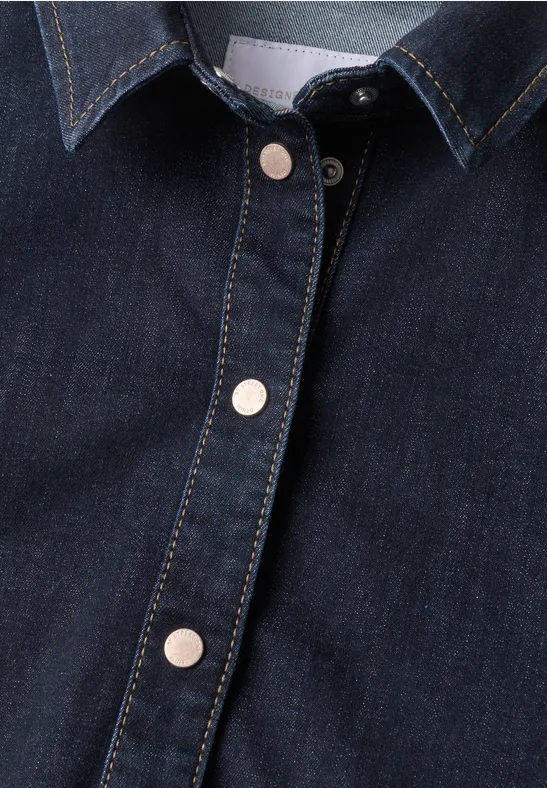 Nahaufnahme eines dunkelblauen Denim-Oberteils mit silbernen Druckknöpfen und kontrastierenden Nähten.