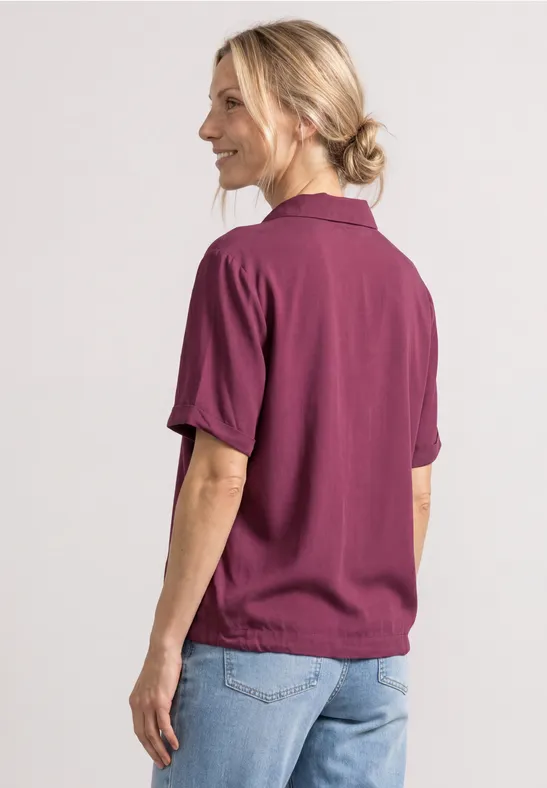 Frau von hinten in beerenfarbenem Shirt und hellen Jeans.