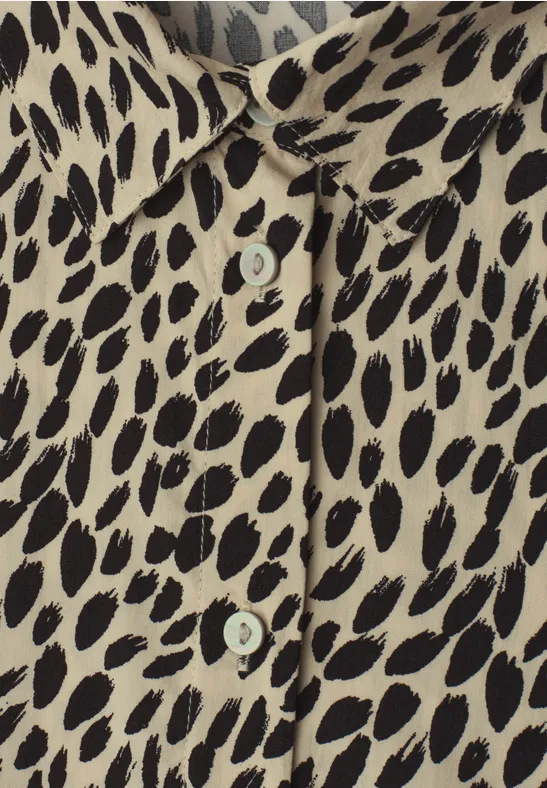 Beige Bluse mit unregelmäßigem schwarzen Leopardenmuster und sichtbaren Knöpfen.