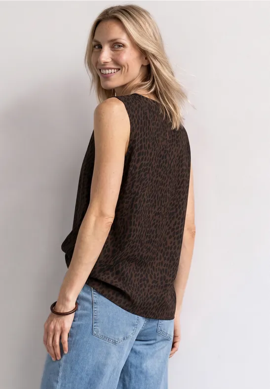 Frau in ärmellosem Oberteil und Jeans lächelnd vor hellem Hintergrund.