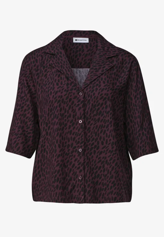 Lockere, lila Bluse mit schwarzem Punktemuster und Knopfleiste.