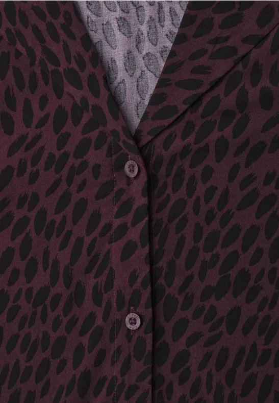 Nahaufnahme eines lila Blazers mit schwarzem Blattmuster und Knöpfen.