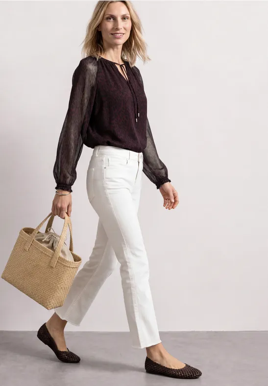Frau in weißer Hose, schwarzer Bluse, trägt beige Tasche und flache Loafers.