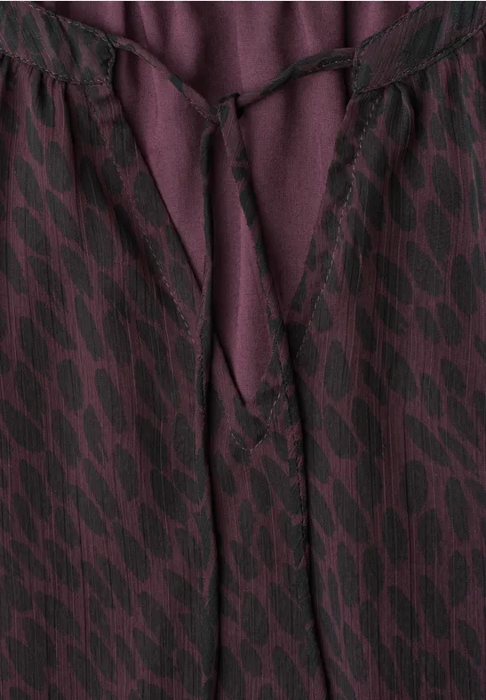Violett-schwarze gemusterte Bluse mit V-Ausschnitt und Stoffband zum Schnüren.