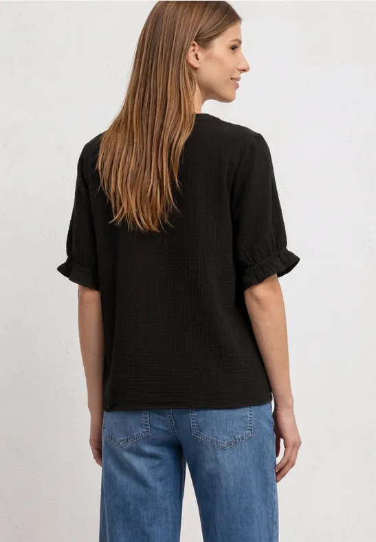 Eine Frau im Profil trägt ein schwarzes Rüschen-T-Shirt und blaue Jeans, Aufnahme von hinten.