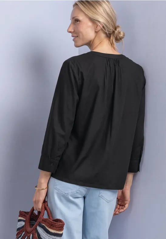 Frau von hinten in schwarzer Bluse, hellen Jeans und mit geflochtener Tasche zu sehen.