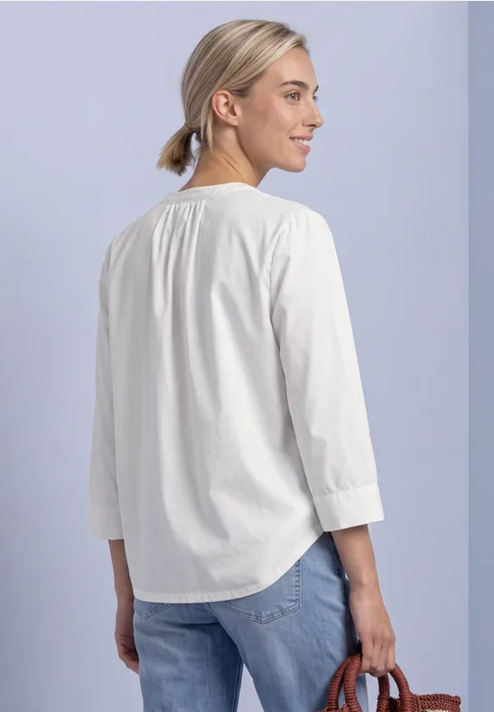 Frau von hinten in weißer 3/4-Arm-Bluse mit blondem Dutt, Jeans und kleiner brauner Tasche.