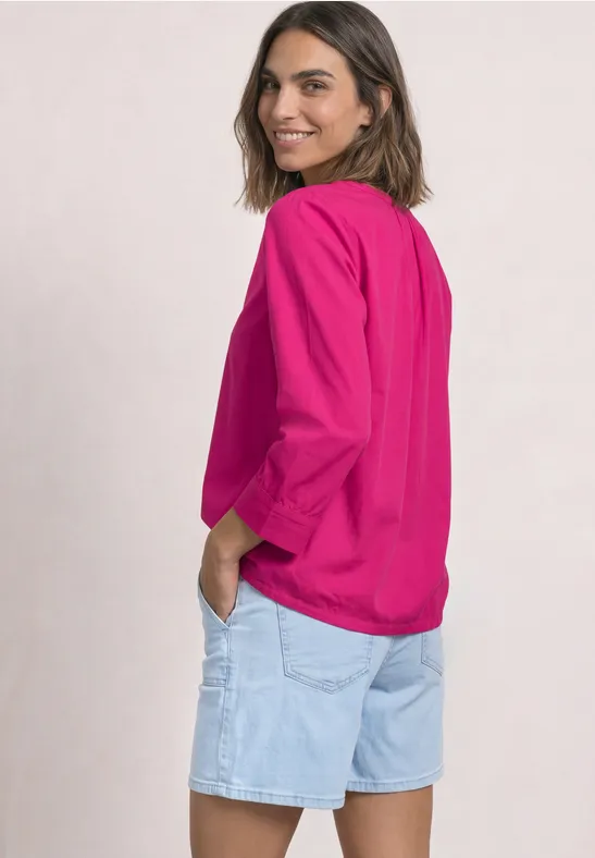 Femme en haut rose et short en jean clair, souriante, regardant par-dessus son épaule.