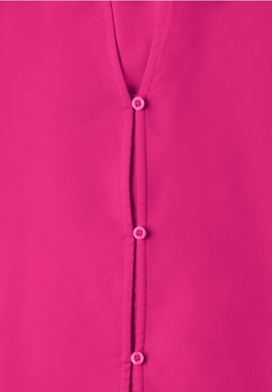 Gros plan sur une blouse rose vif à trois boutons.