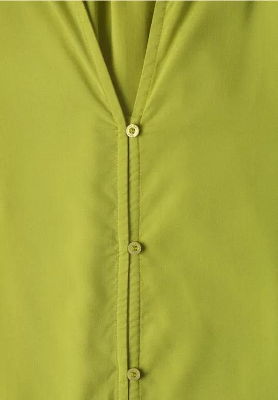 Gros plan sur une chemise vert clair à boutons apparents et coutures visibles.