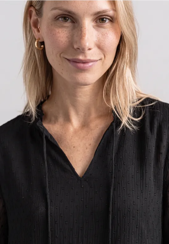 Uśmiechnięta blondynka w czarnej bluzce z piegami na jasnym tle.