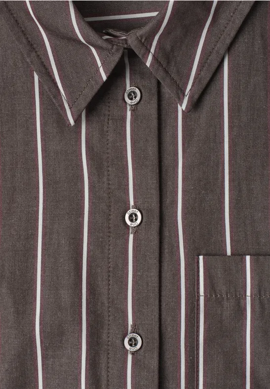 Gros plan sur une chemise gris foncé à fines rayures blanches et rouges, boutons et poche poitrine.