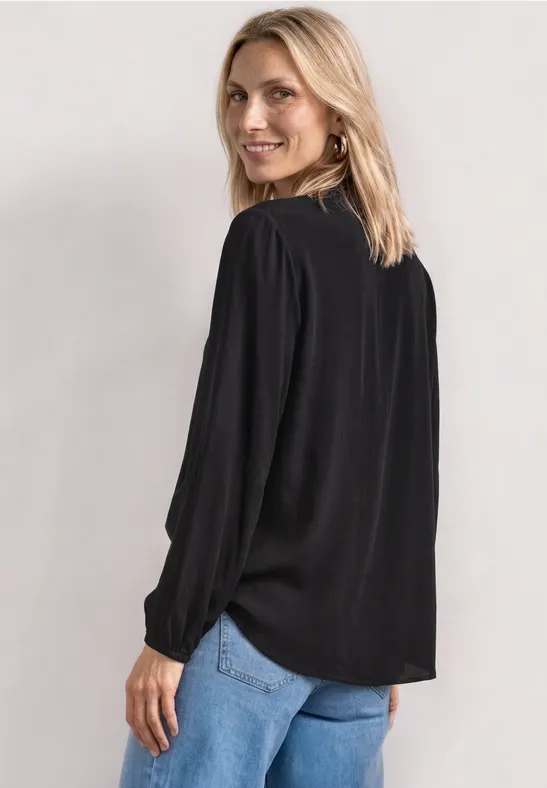Frau von hinten in einer schwarzen Bluse mit Zierperlen und blauen Jeans