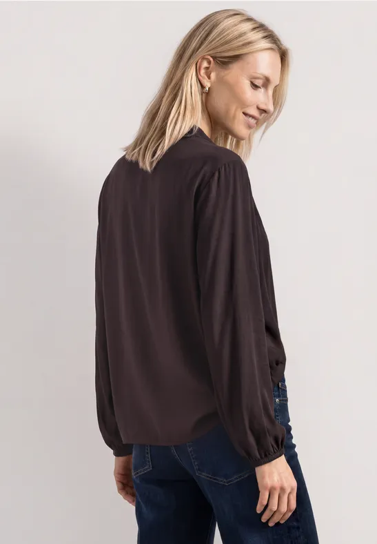 Frau von hinten in schwarzer Bluse und Jeans, lange Ärmel, lockere Passform.