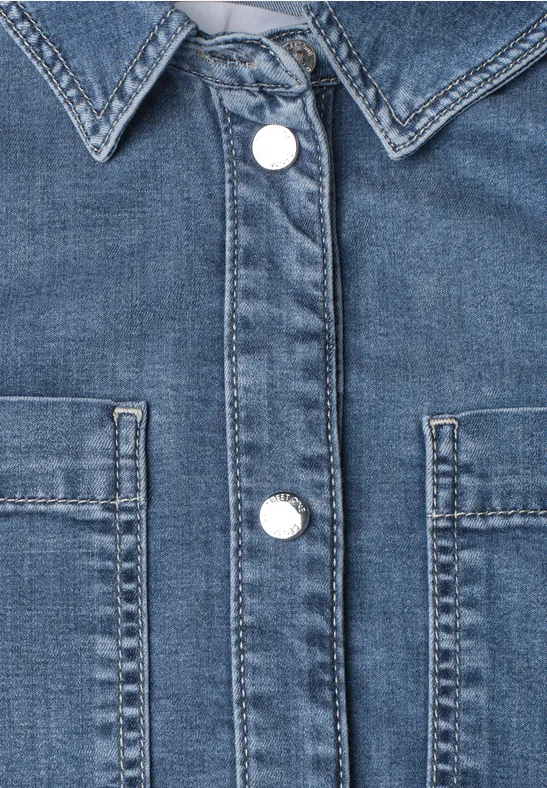 Nahaufnahme einer blauen Jeansjacke mit Kragen, weißen Druckknöpfen und zwei Brusttaschen.