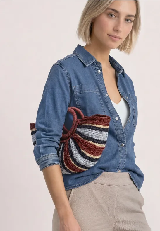 Frau trägt Jeanshemd und helle Hose, hält bunt gestreifte Tasche lässig unter dem Arm.