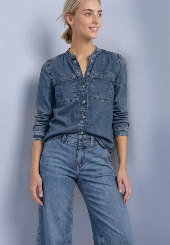 Jeansbluse und Jeanshose an entspannter Frau vor neutralem Hintergrund