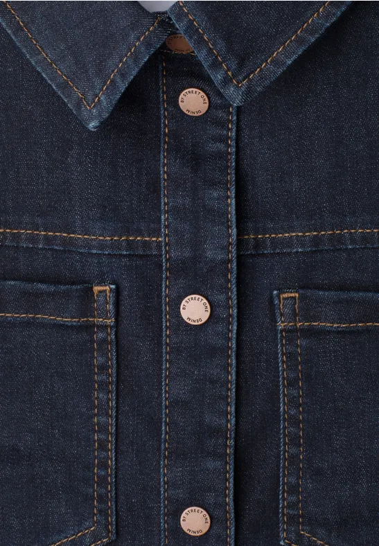 Nahaufnahme einer blauen Jeansjacke mit Kragen, Knopfleiste und aufgesetzten Taschen.