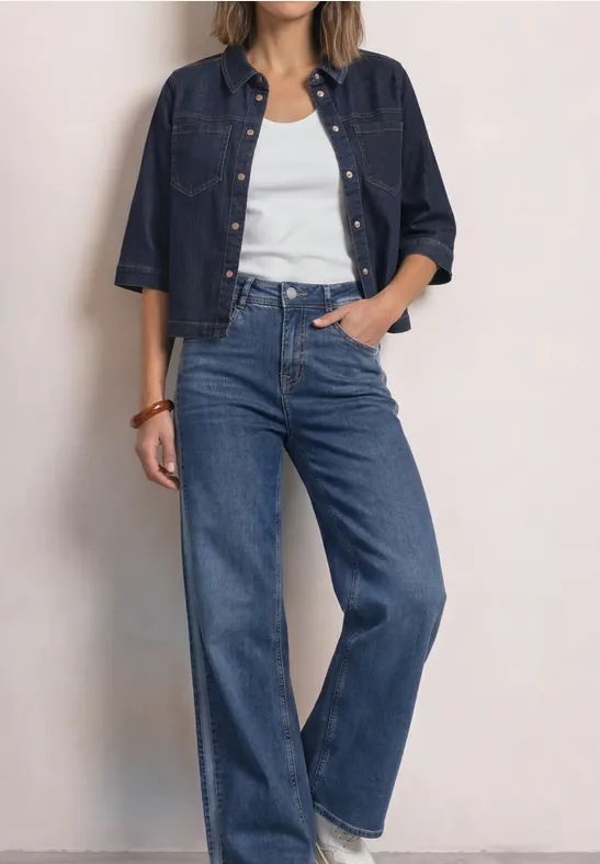 Frau trägt weißes Tanktop, weite blaue High-Waist-Jeans und dunkelblaue Jeansjacke.