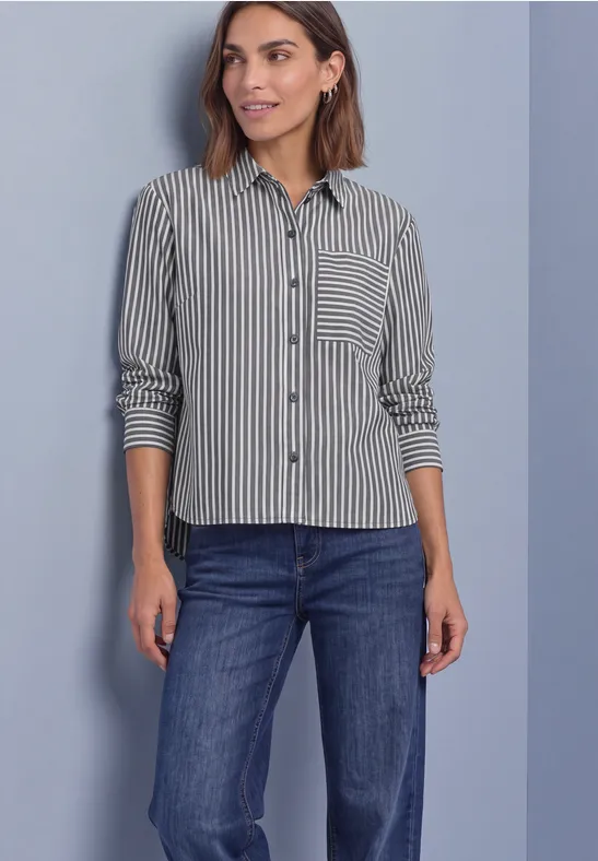 Femme portant une chemise rayée noir et blanc et un jean bleu devant un fond clair.