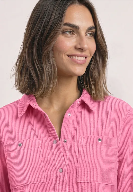 Porträt einer lächelnden Frau mit schulterlangem braunen Haar und pinker Cord-Hemdbluse.