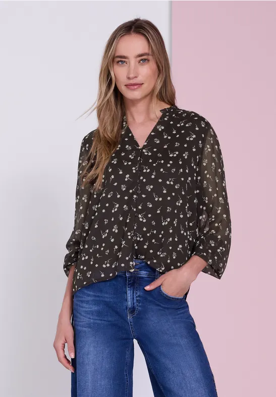 Vrouw in een donkerblouse met patroontjes en blauwe jeans voor een tweekleurige roze achtergrond.