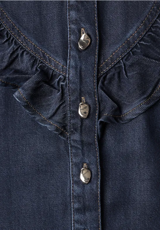 Nahaufnahme eines dunkelblauen Jeansoberteils mit Metallknöpfen und Rüschen.