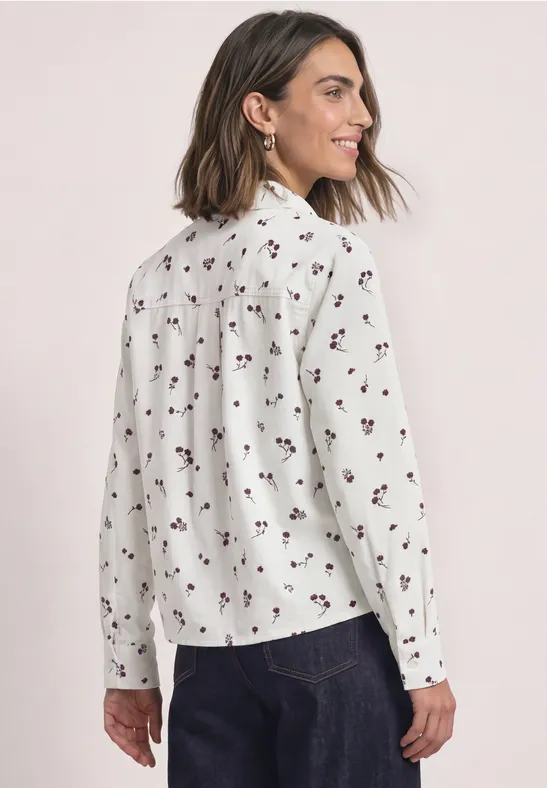 Frau von hinten in weißer Bluse mit kleinem Blumenmuster und dunkler Hose.