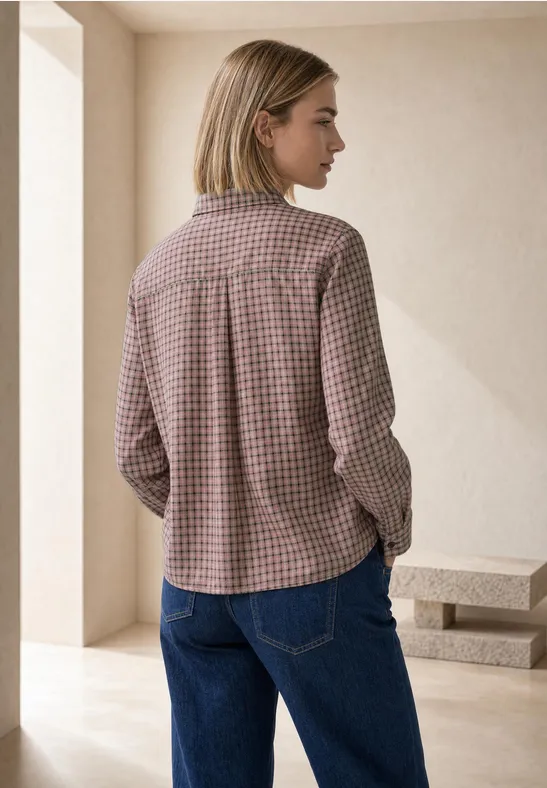 Frau von hinten in kariertem Hemd und blauen Jeans vor schlichter Wand.