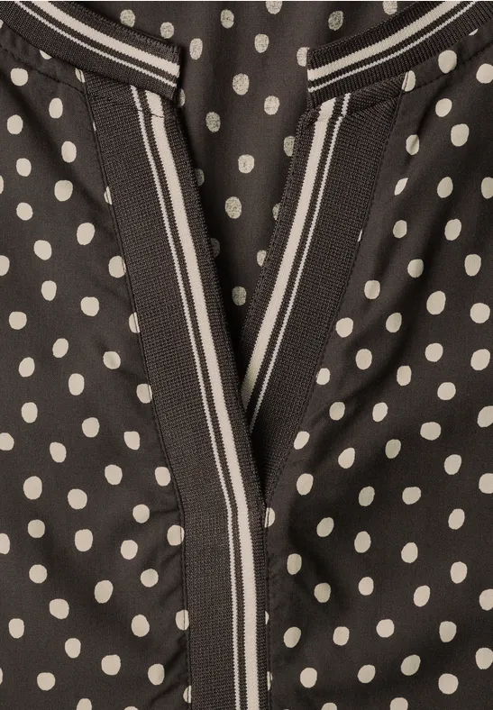 Schwarzes Kleidungsstück mit weißen Polka Dots und V-förmiger Nahtöffnung.