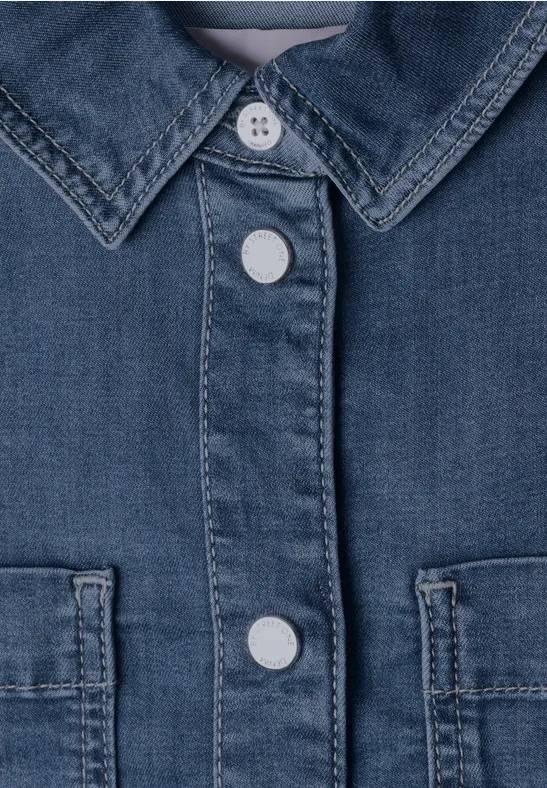 Nahaufnahme eines blauen Jeanshemds mit sichtbaren weißen Knöpfen und Brusttaschen.