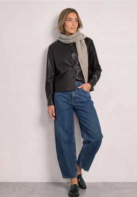 Frau trägt schwarze Lederjacke, grauen Schal, weite Jeans und schwarze Loafers.