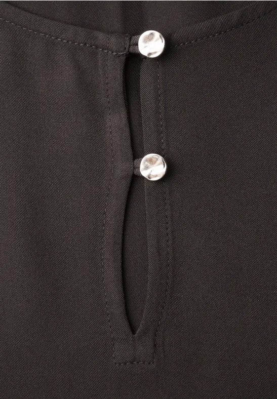 Schwarzes Oberteil mit Knopfleiste und zwei silbernen Knöpfen.