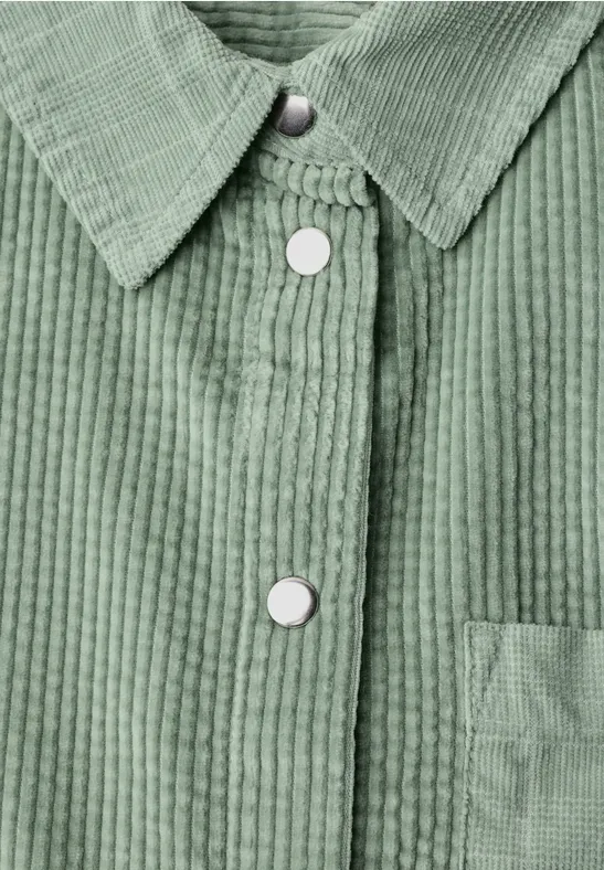 Grüne Cordjacke mit weißen Druckknöpfen und aufgesetzter Tasche.