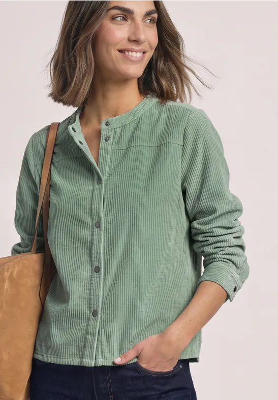 Lächelnde Frau in grüner Hemdjacke mit Beutel über der Schulter.